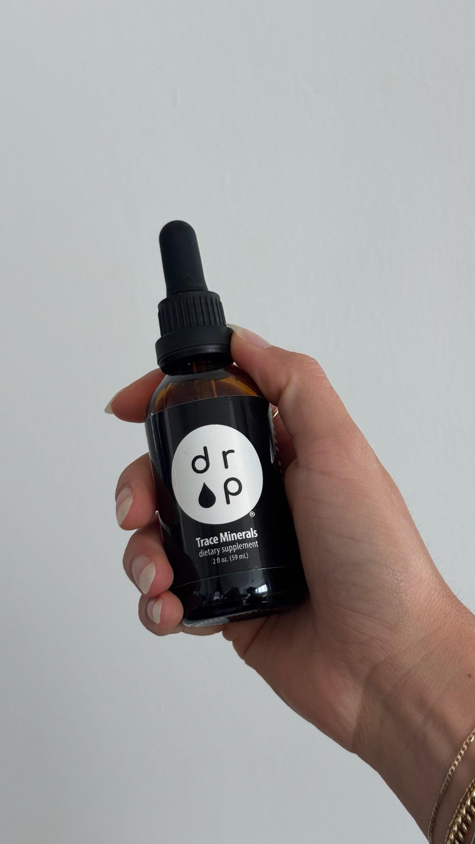 Hand holding a black bottle labeled 'drop' against a light gray background